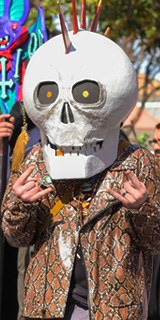A guy wearing a large skull mask with a spikey mohawk.